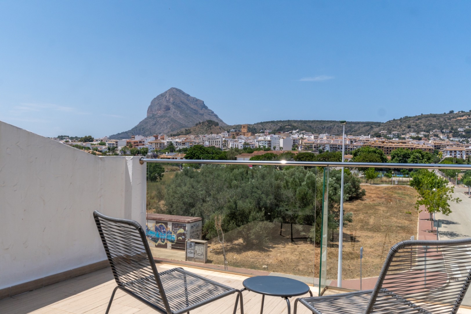 Terraza superior con barandilla de cristal y vistas panorámicas despejadas al Montgó y al casco antiguo de Jávea. Incluye mobiliario de exterior moderno sobre suelo cerámico.