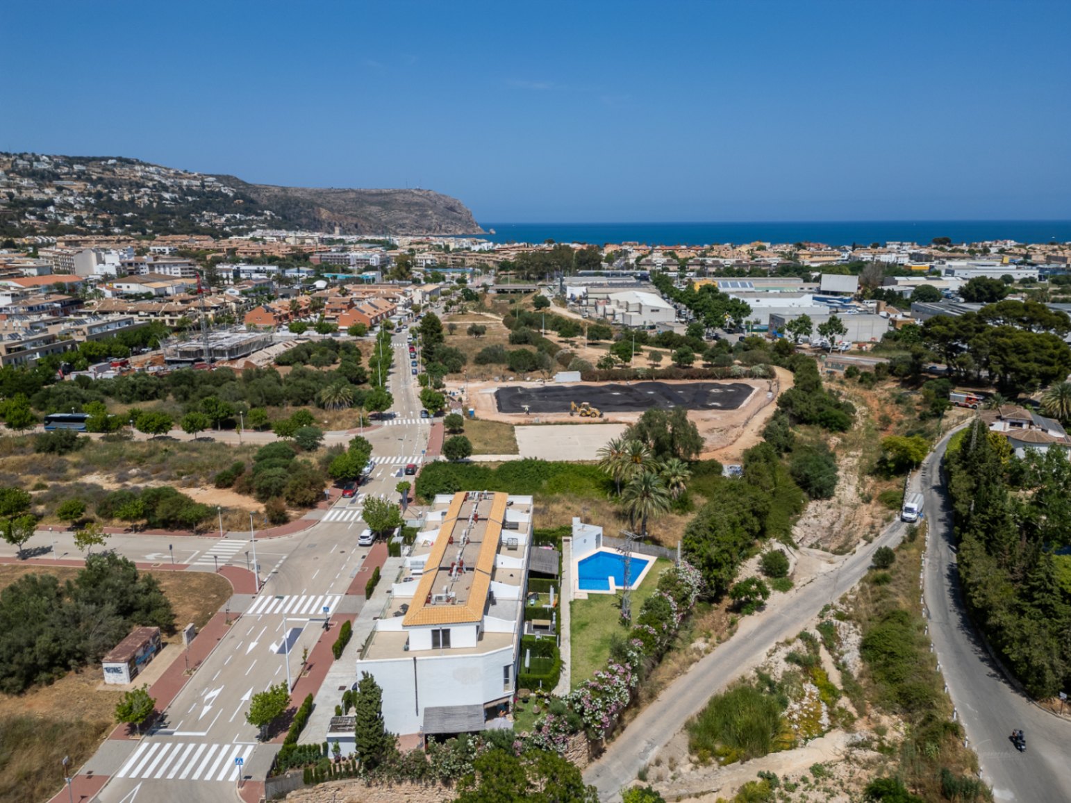 Vista aérea de la urbanización moderna con piscina comunitaria, mostrando su ubicación estratégica cerca del mar y el entorno residencial en expansión de Jávea.