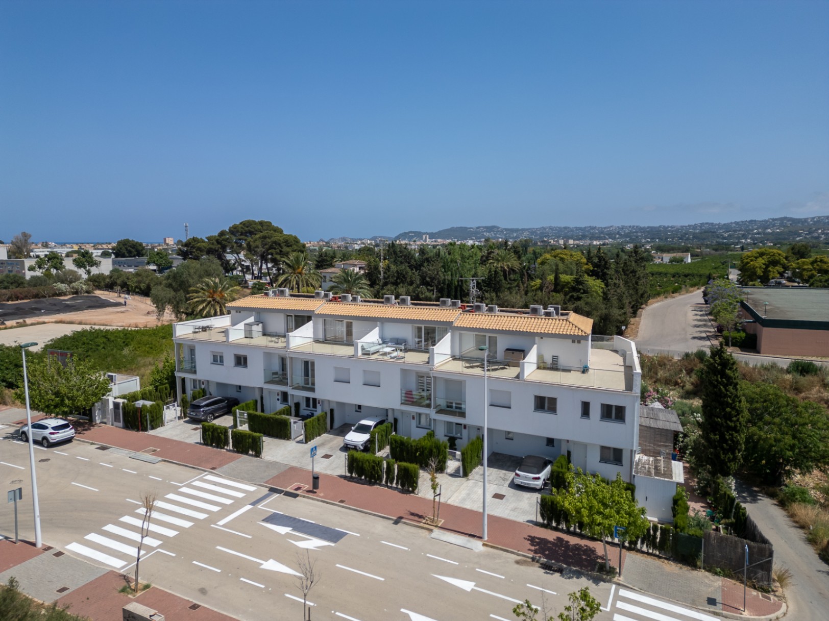 Vista exterior de la hilera de casas adosadas modernas con fachadas blancas, terrazas privadas con barandillas de cristal y plazas de aparcamiento individuales en la entrada.