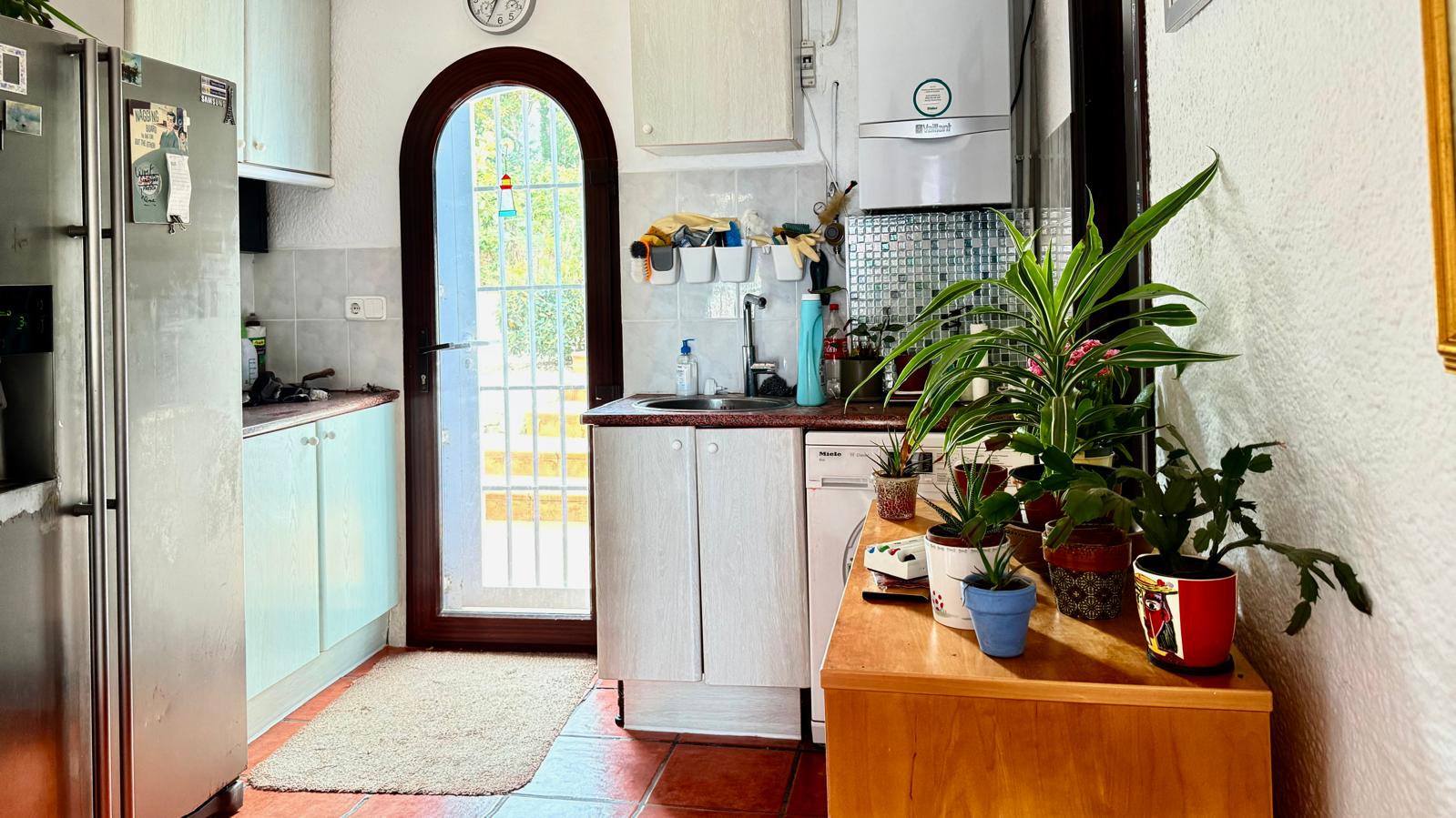Cocina funcional con puerta de arco acristalada, encimeras de granito y suelos de terracota. Dispone de mobiliario blanco, zona de lavadero y abundante luz natural.
