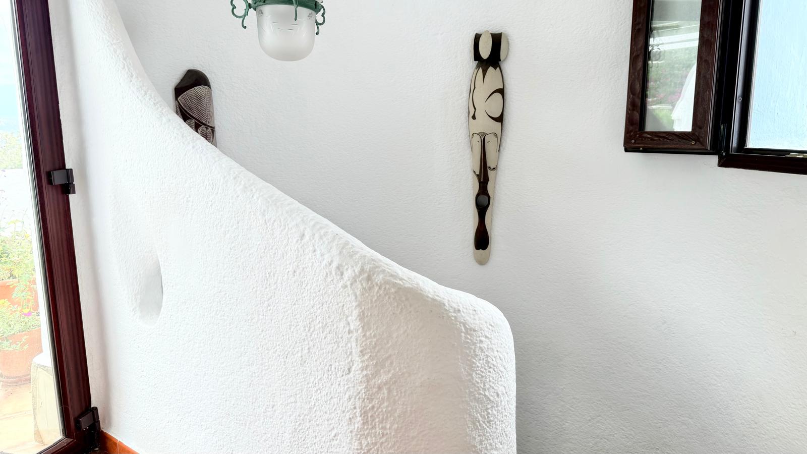 Detalle de la escalera interior curva con paredes de acabado rugoso blanco, reflejando el estilo ibicenco y la arquitectura orgánica de la vivienda.