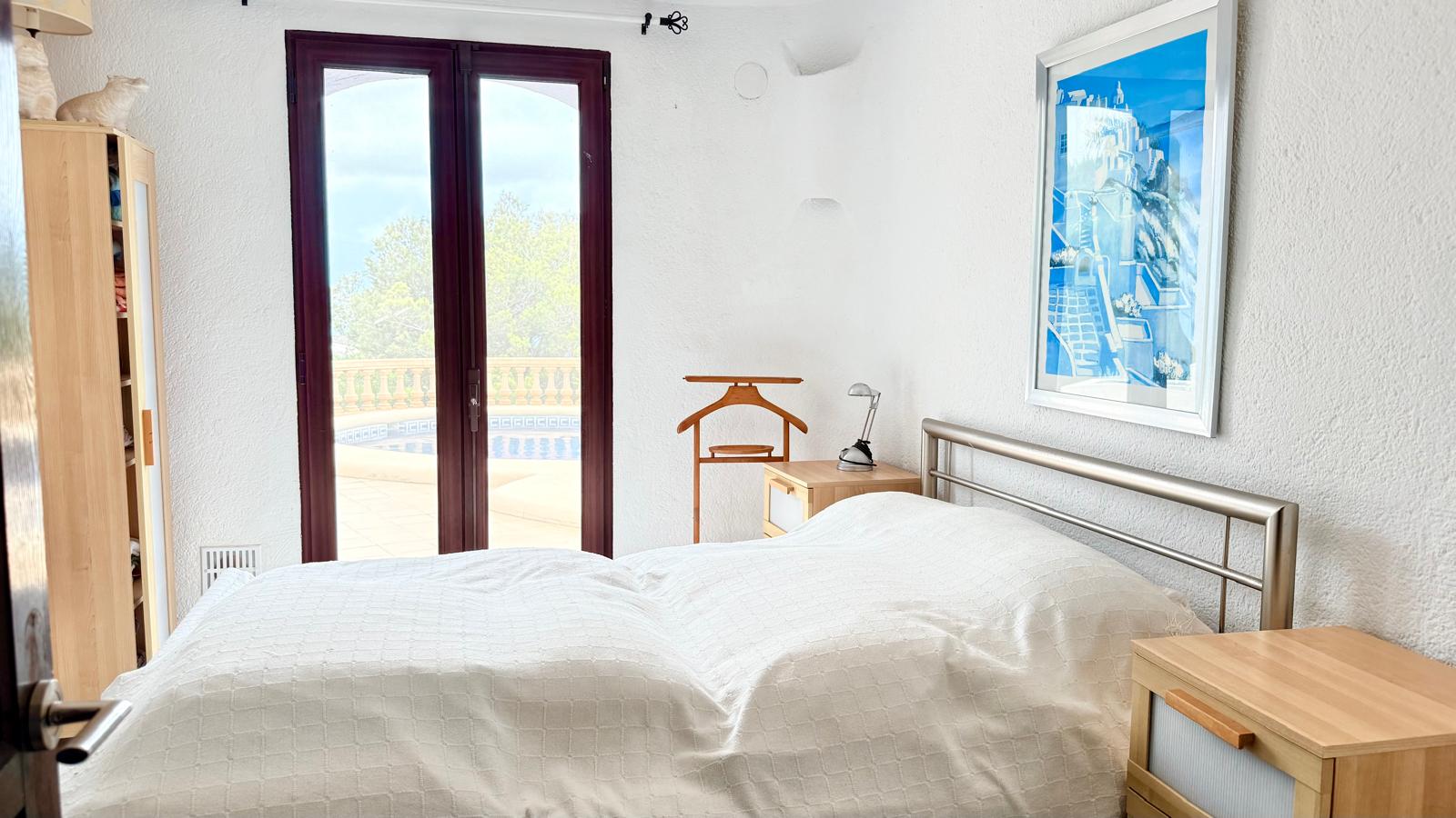 Dormitorio con acceso directo a la zona de piscina, paredes blancas de estilo mediterráneo y mobiliario funcional de madera clara.