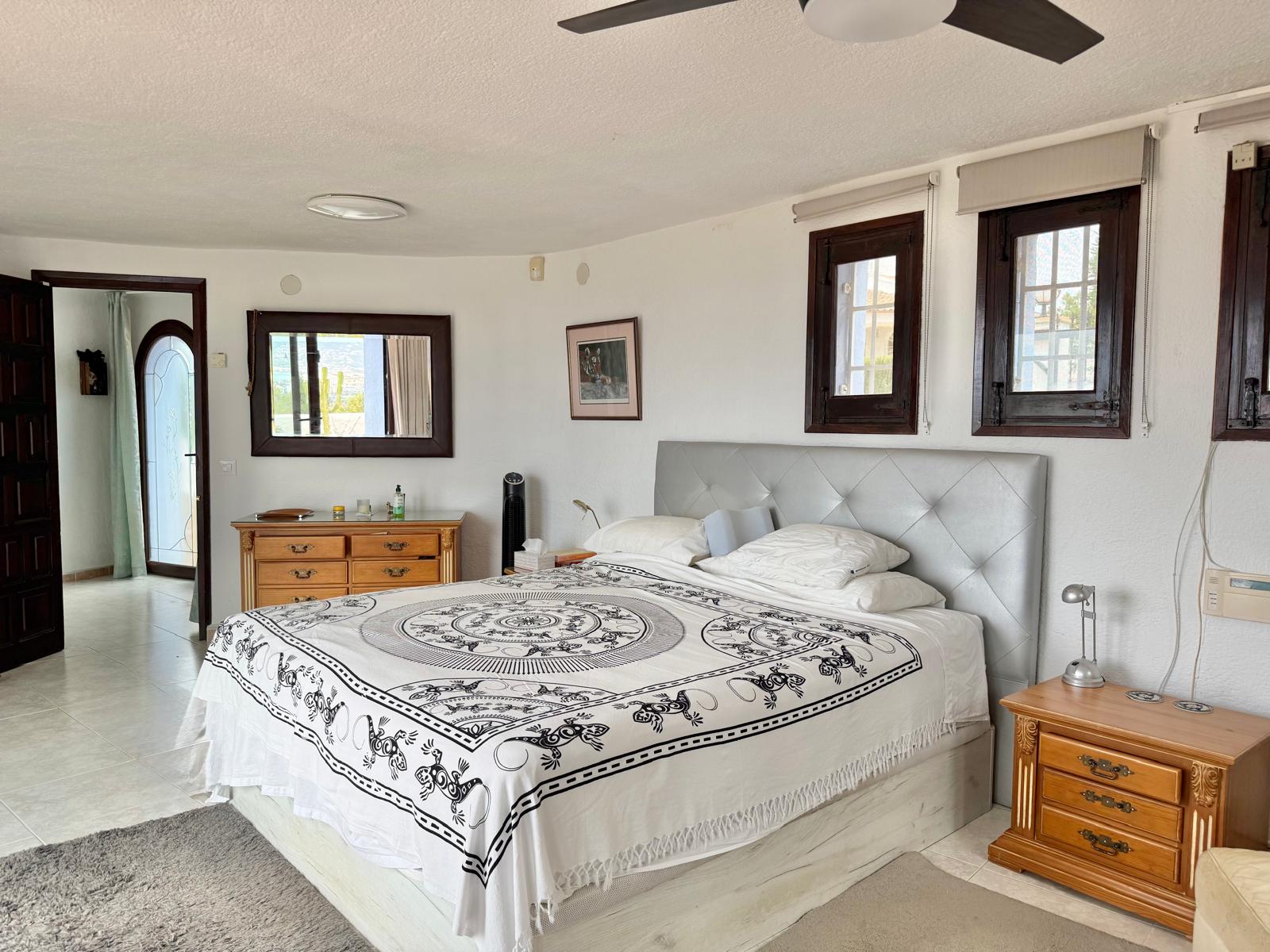 Dormitorio principal con paredes blancas, carpintería de madera oscura y ventilador de techo. Dispone de muebles de madera de estilo clásico y acceso a la zona de vestidor.