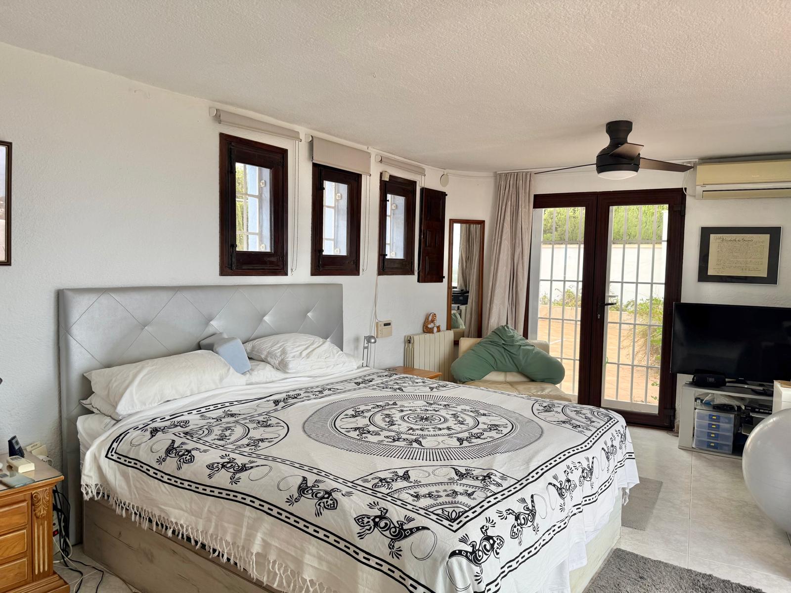 Dormitorio principal luminoso con carpintería de madera oscura, ventilador de techo y acceso directo a la terraza a través de puertas acristaladas.