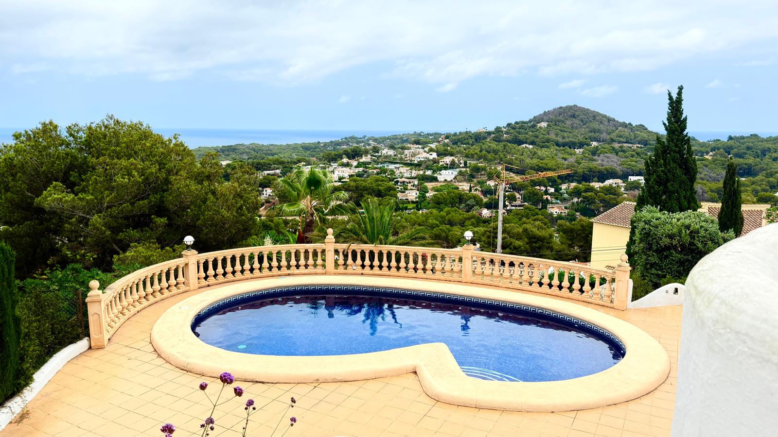 Piscina privada de forma curva rodeada por una terraza de gres y balaustrada clásica, con vistas panorámicas al mar Mediterráneo y al entorno natural de Jávea.