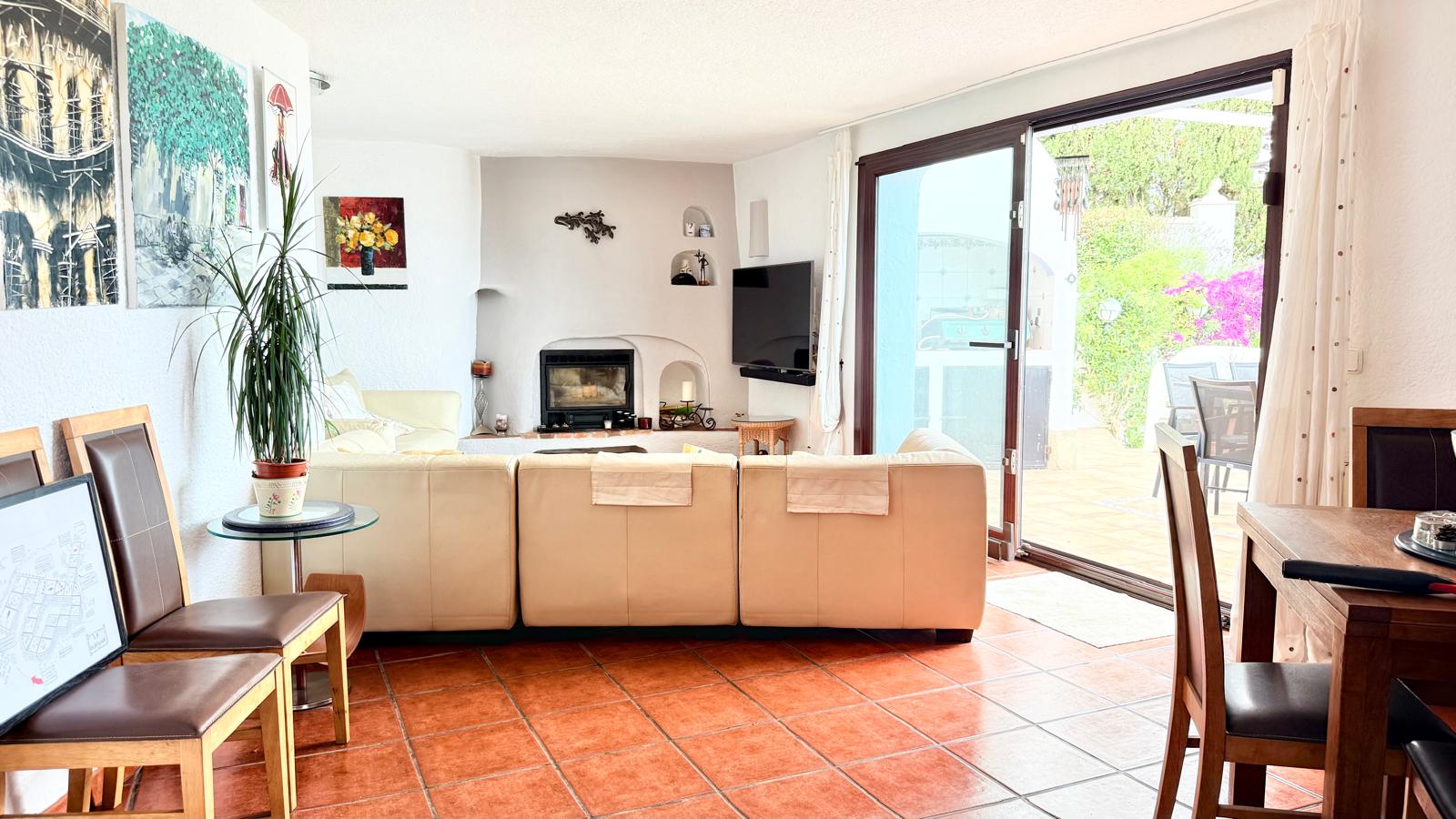 Salón-comedor con chimenea de leña integrada, suelos de gres rústico y acceso directo a la terraza mediante un gran ventanal corredero que aporta luz natural.