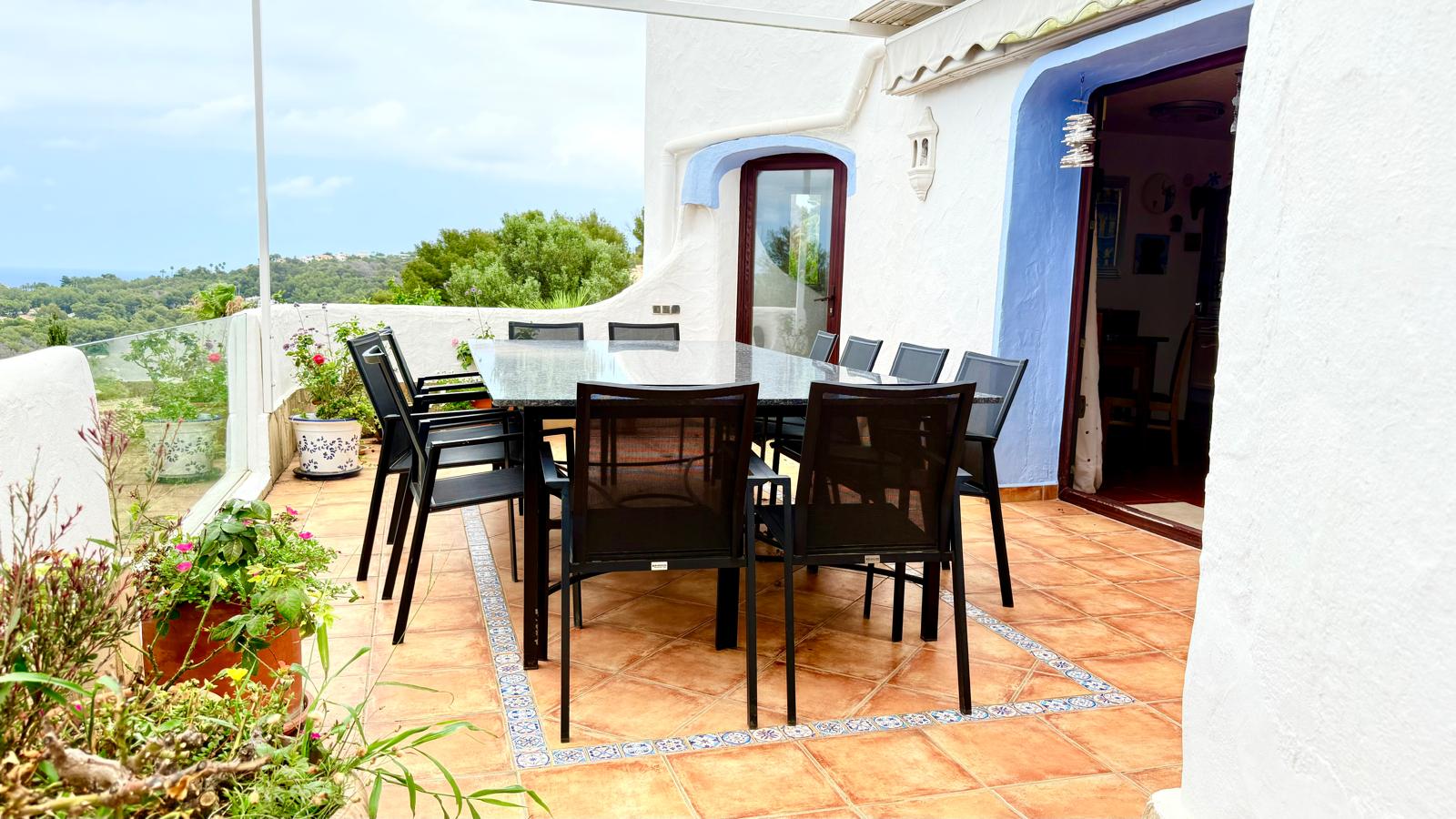 Terraza principal con comedor exterior, mesa de granito y suelos de barro con cenefas decorativas. Ofrece vistas abiertas al mar y acceso directo a la vivienda.