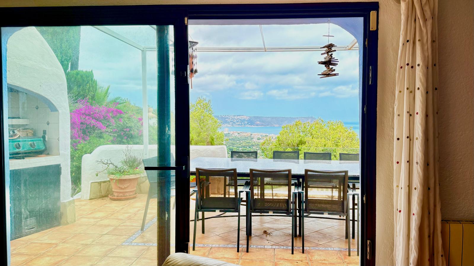 Vista desde el salón hacia la terraza principal, que cuenta con comedor exterior, barbacoa integrada y vistas panorámicas a la bahía de Jávea y el mar Mediterráneo.