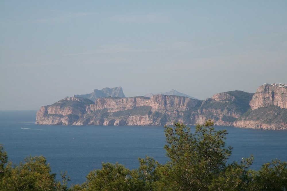 Vistas panorámicas al mar Mediterráneo y a los acantilados de piedra caliza desde la parcela, con pinos autóctonos en primer plano.