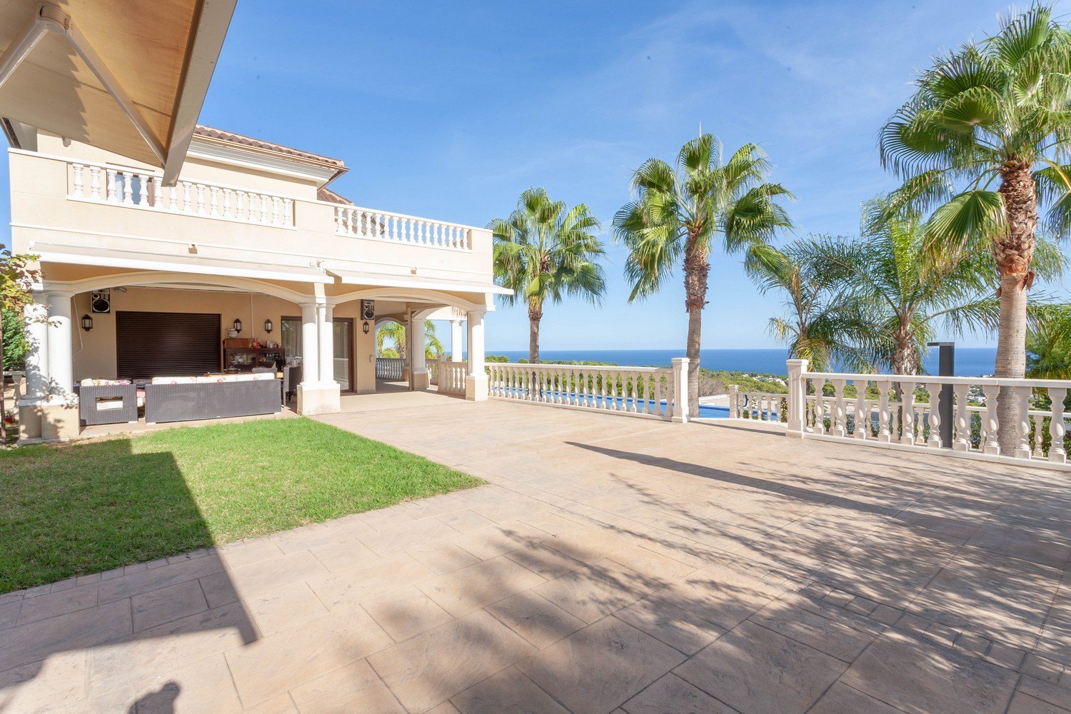 Amplia terraza con vistas al mar y piscina, realzada por palmeras y balaustrada clásica.