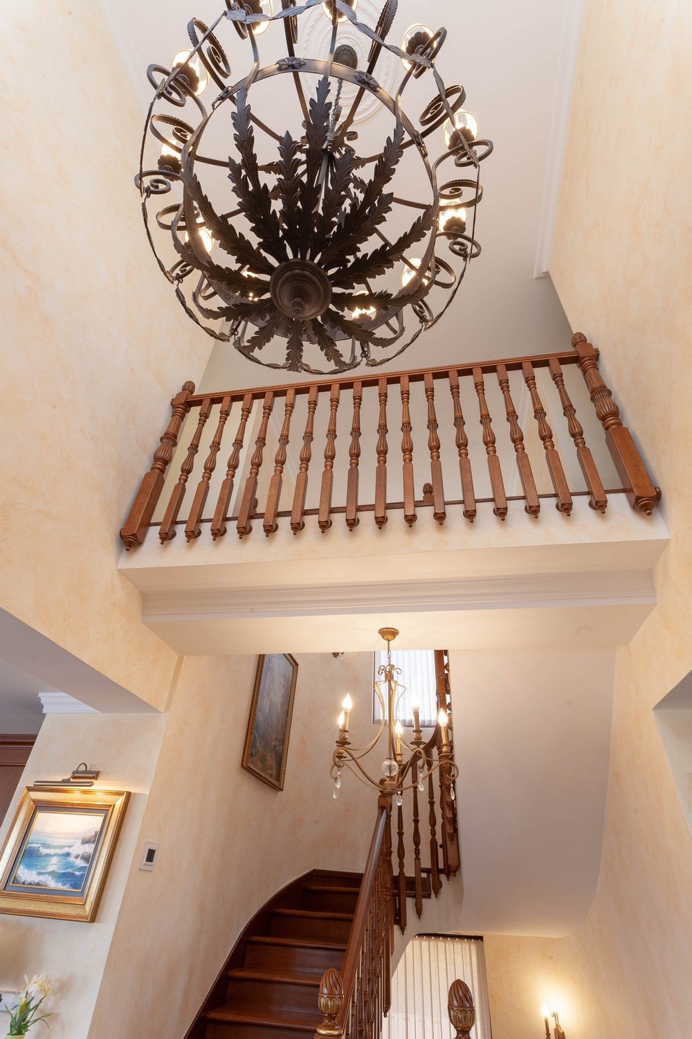 Detalle de la escalera de madera con barandilla y lámpara de araña decorativa.
