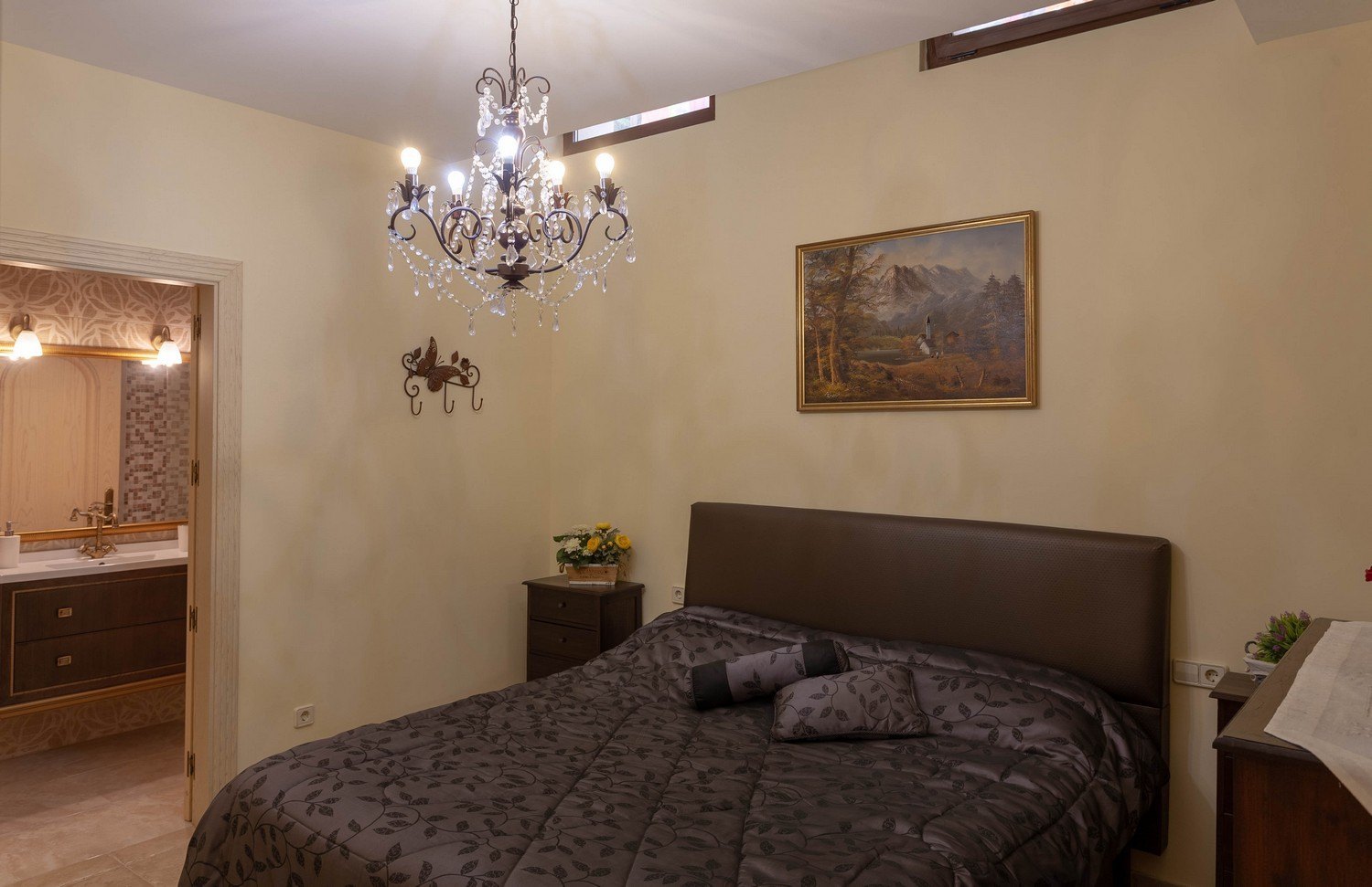 Dormitorio con cama doble, lámpara de araña de cristal y acceso al baño en suite con lavabo doble.