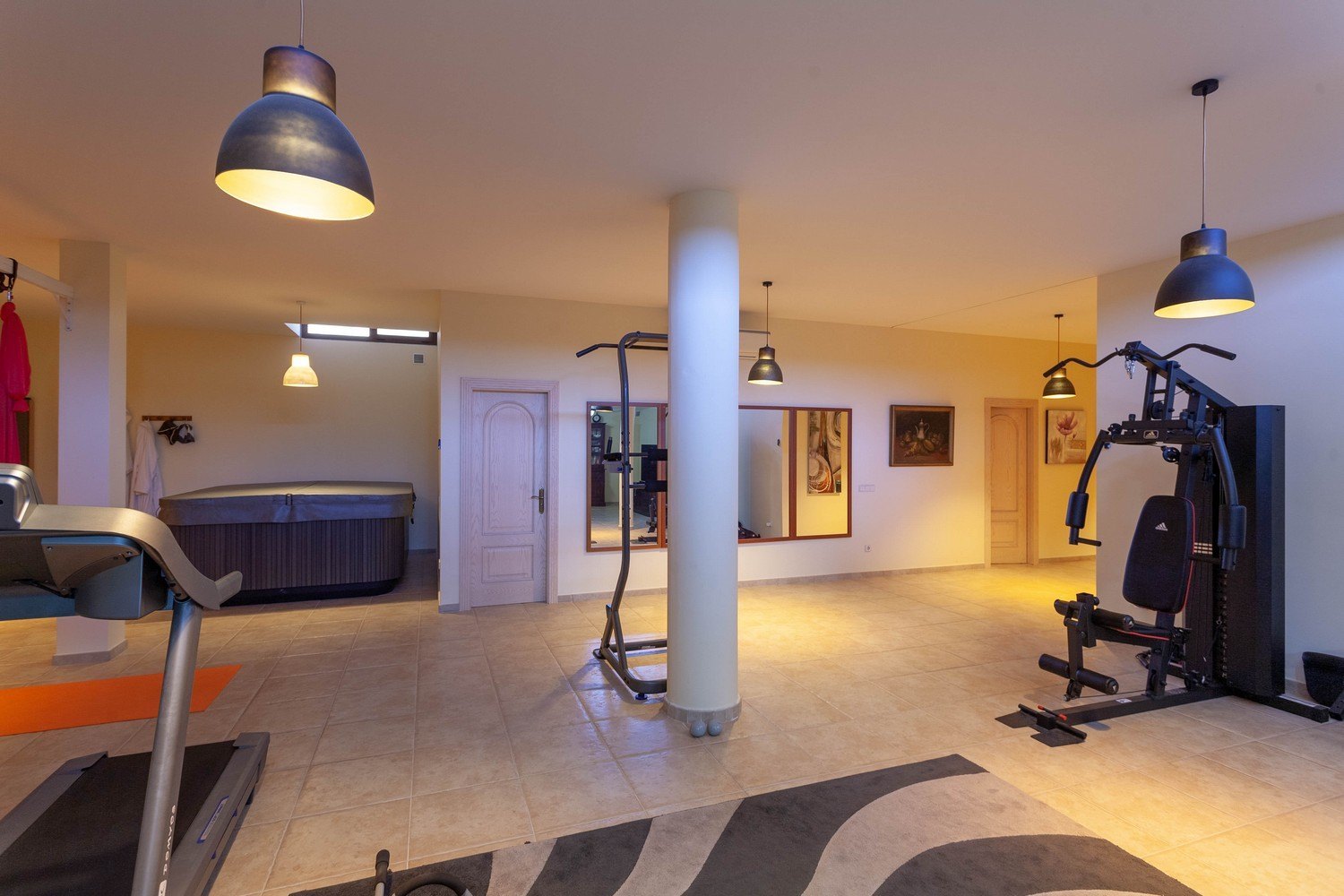 Gimnasio con jacuzzi, suelo de baldosas color crema y luz ambiental cálida.