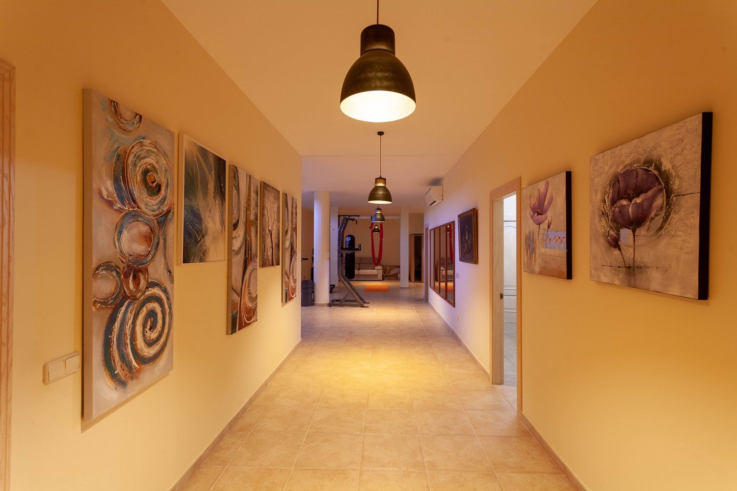 Pasillo iluminado con obras de arte y acceso al gimnasio.