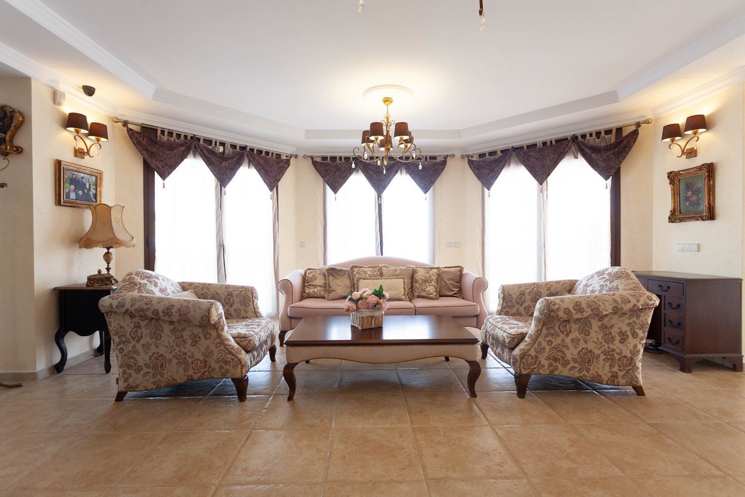 Salón con sofás florales y mesa de centro de madera, iluminado por luz natural y lámpara de araña.