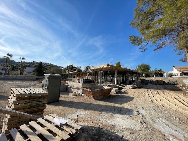 Construcción de villa en Moraira: estructura de hormigón con soportes metálicos bajo cielo azul.