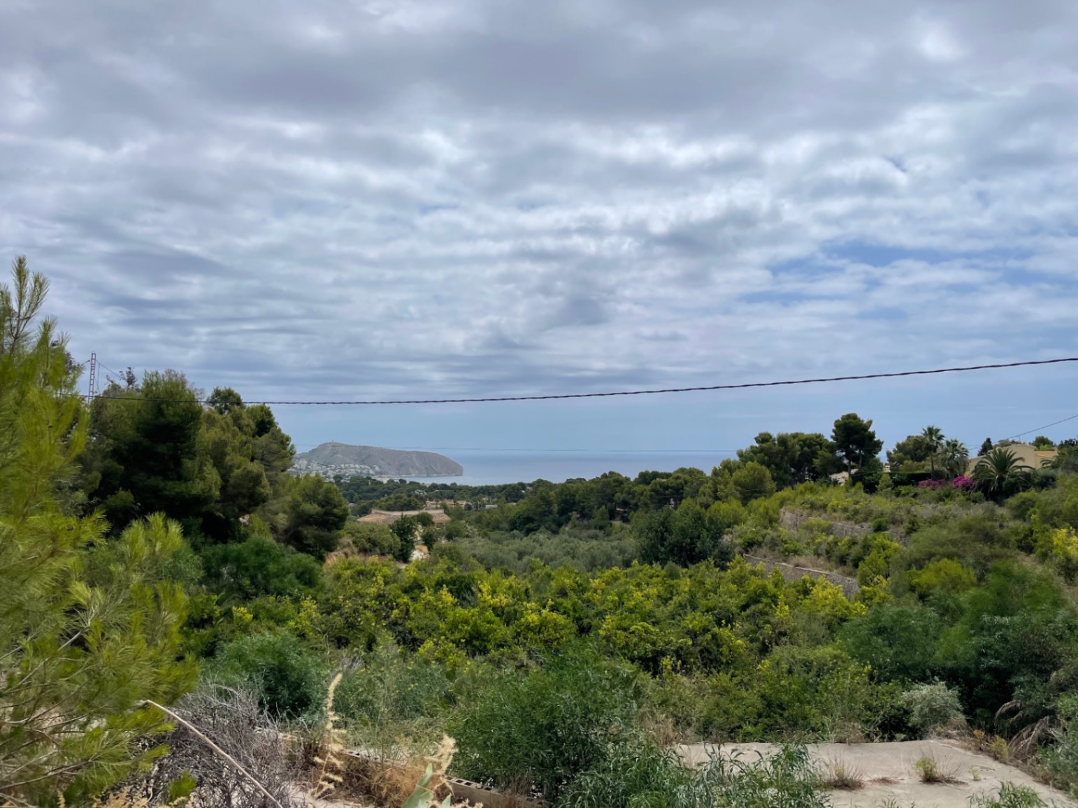 Vista panorámica al mar Mediterráneo y al cabo desde la parcela elevada, rodeada de vegetación autóctona y pinos en Benimeit, Moraira.