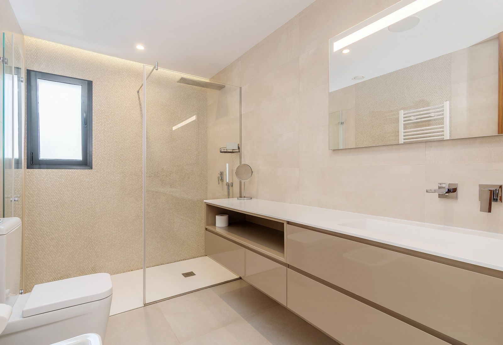 Baño moderno con ducha italiana, mampara de cristal y pared de mosaico. Incluye mueble suspendido en tonos beige, lavabo integrado y espejo con iluminación LED.