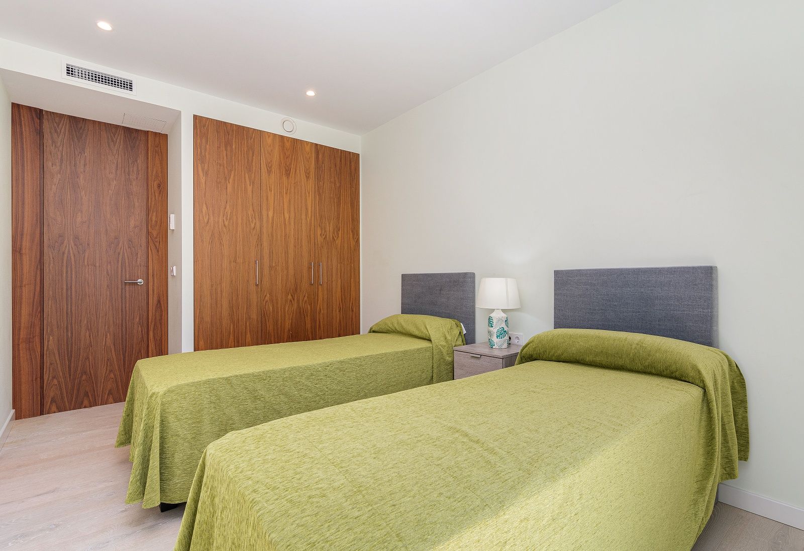 Dormitorio luminoso con dos camas individuales, armarios empotrados de madera natural y aire acondicionado por conductos integrado en el techo.