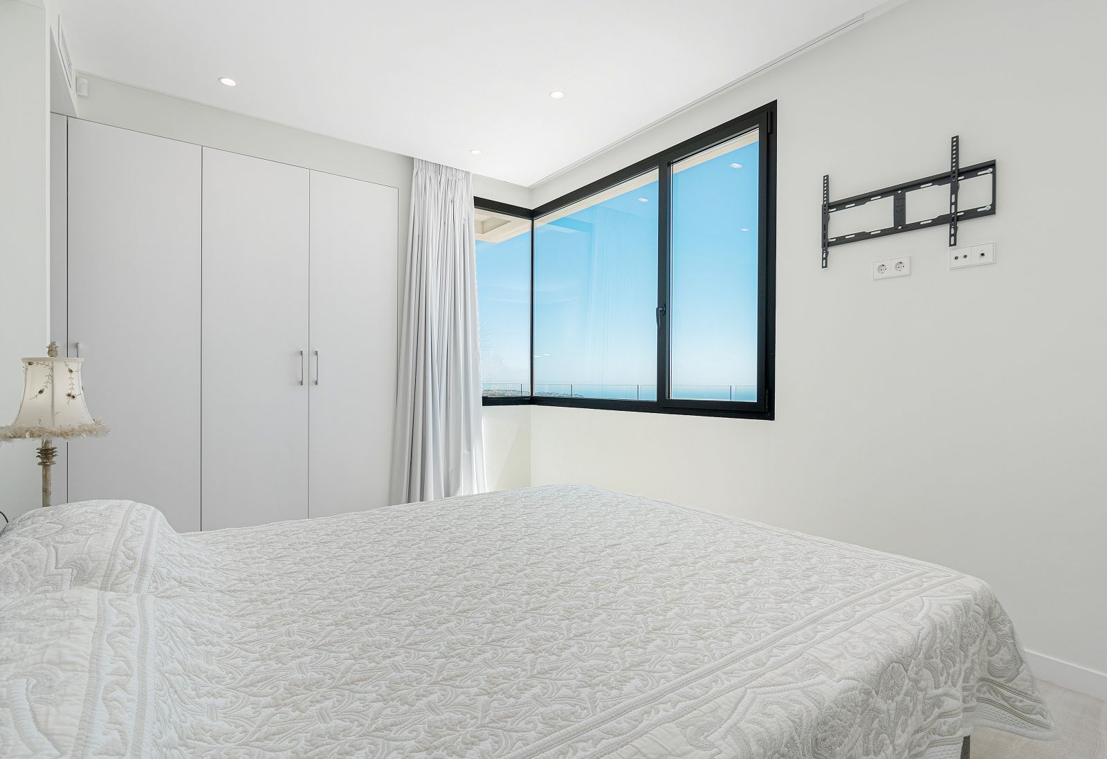 Dormitorio moderno con armarios empotrados blancos, ventanal de esquina con marcos negros y vistas panorámicas al mar Mediterráneo.