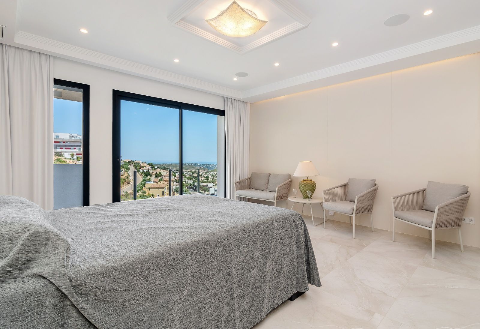 Dormitorio principal con suelos de mármol, zona de estar integrada y grandes ventanales con vistas panorámicas al mar y a la urbanización Cumbre del Sol.