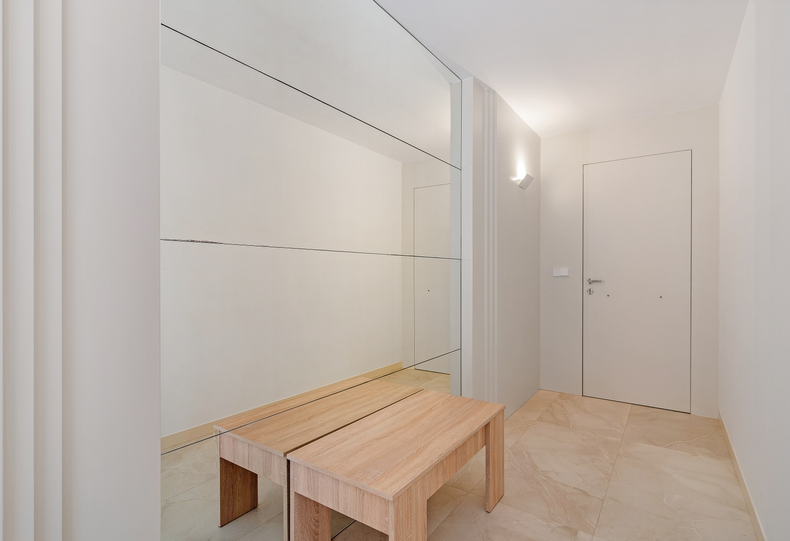 Pasillo de entrada minimalista con gran espejo de pared, banco de madera clara y suelos de gres porcelánico en tonos crema.