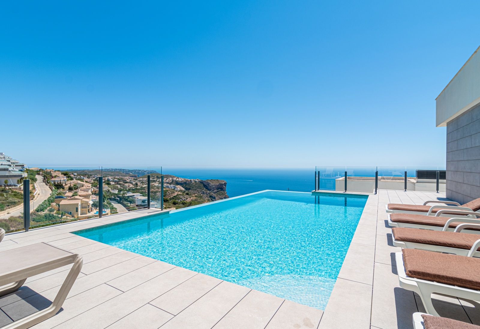 Piscina infinita con vistas panorámicas al mar Mediterráneo, rodeada de una terraza de gres porcelánico y barandillas de cristal de seguridad.