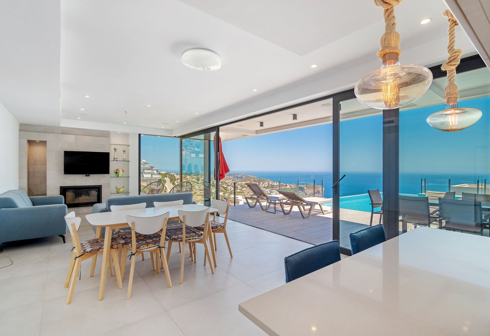 Salón-comedor diáfano con grandes ventanales que conectan con la terraza, piscina infinita y vistas panorámicas al mar Mediterráneo.