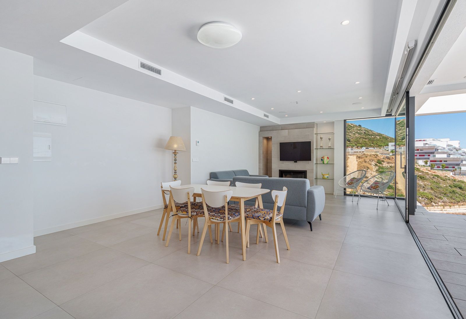 Salón comedor diáfano con suelos de gres porcelánico, aire acondicionado por conductos y grandes ventanales con acceso directo a la terraza y vistas despejadas.