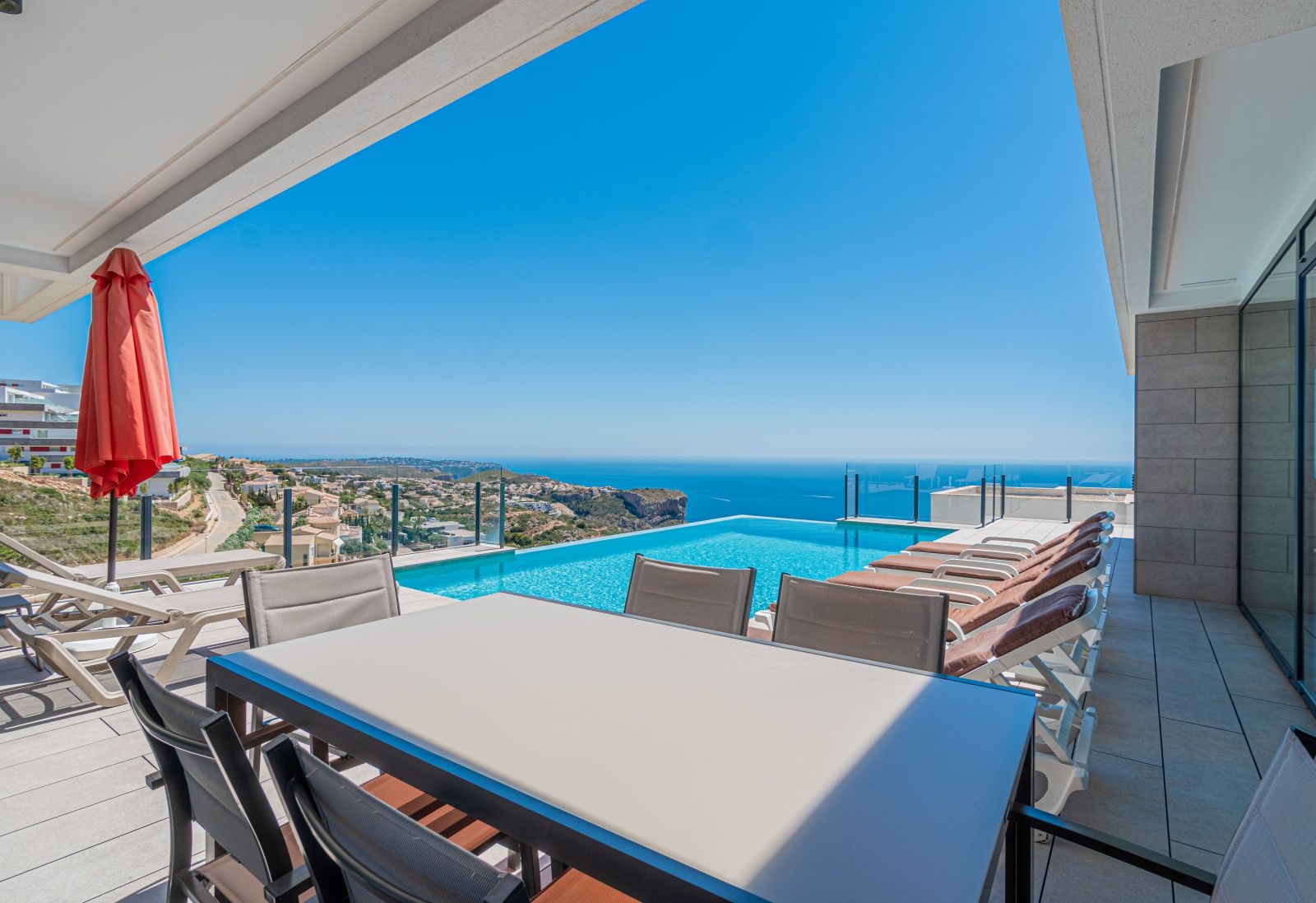 Terraza principal con piscina infinita, zona de comedor exterior y vistas panorámicas al mar Mediterráneo y los acantilados de Cumbre del Sol.