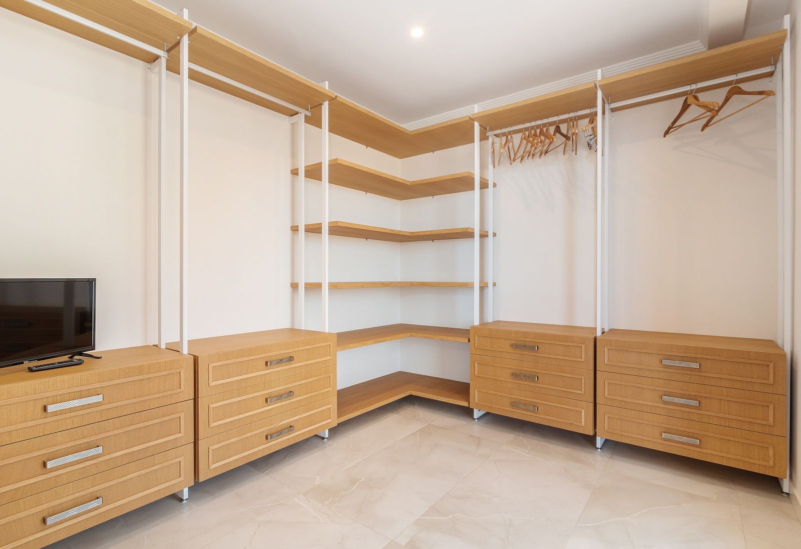 Vestidor abierto con estanterías de madera clara, cajoneras integradas y suelo porcelánico de efecto mármol con iluminación cenital empotrada.