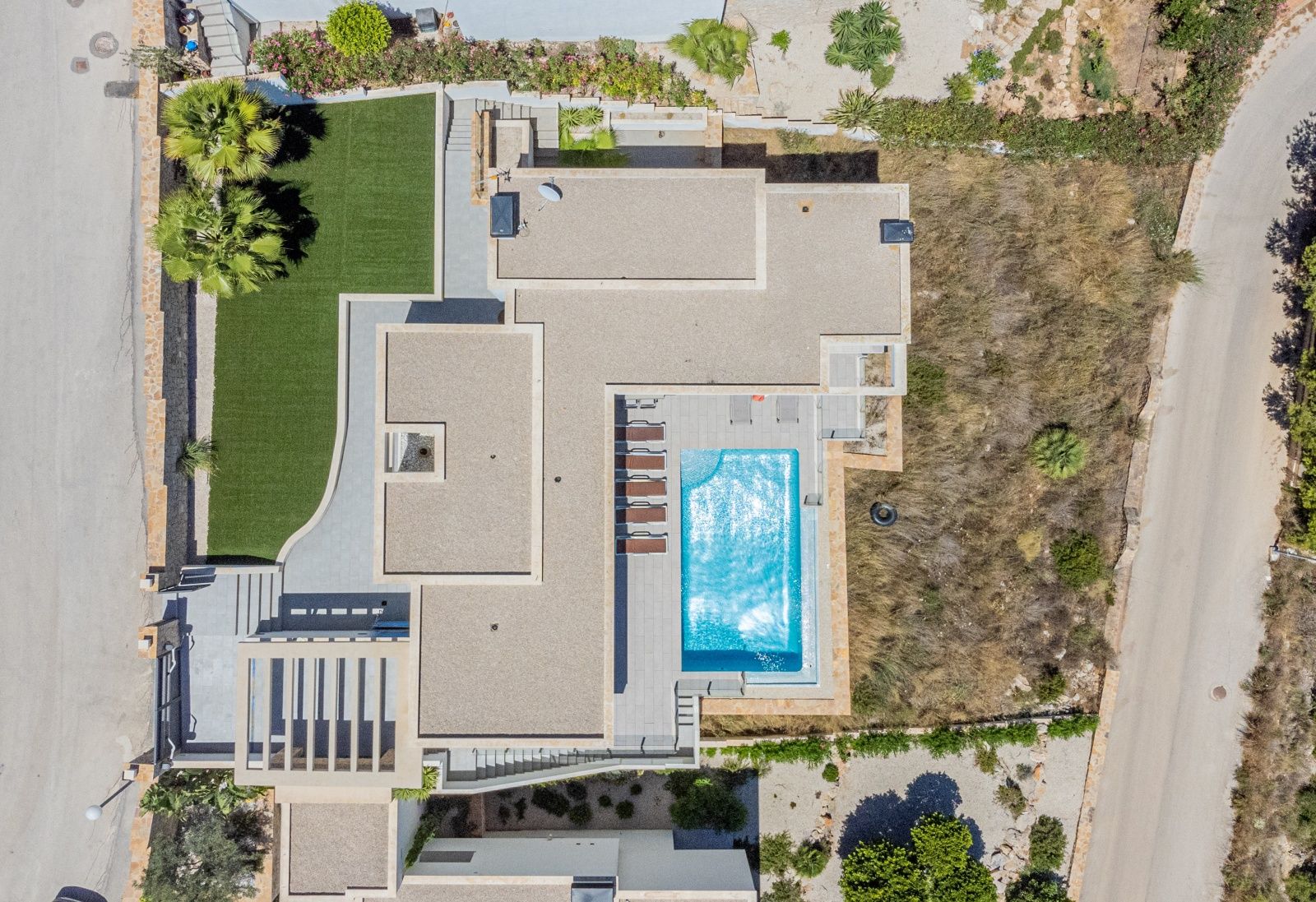 Vista aérea cenital de la villa moderna que muestra la distribución de la parcela, la piscina rectangular con solárium y el jardín perimetral con césped artificial.