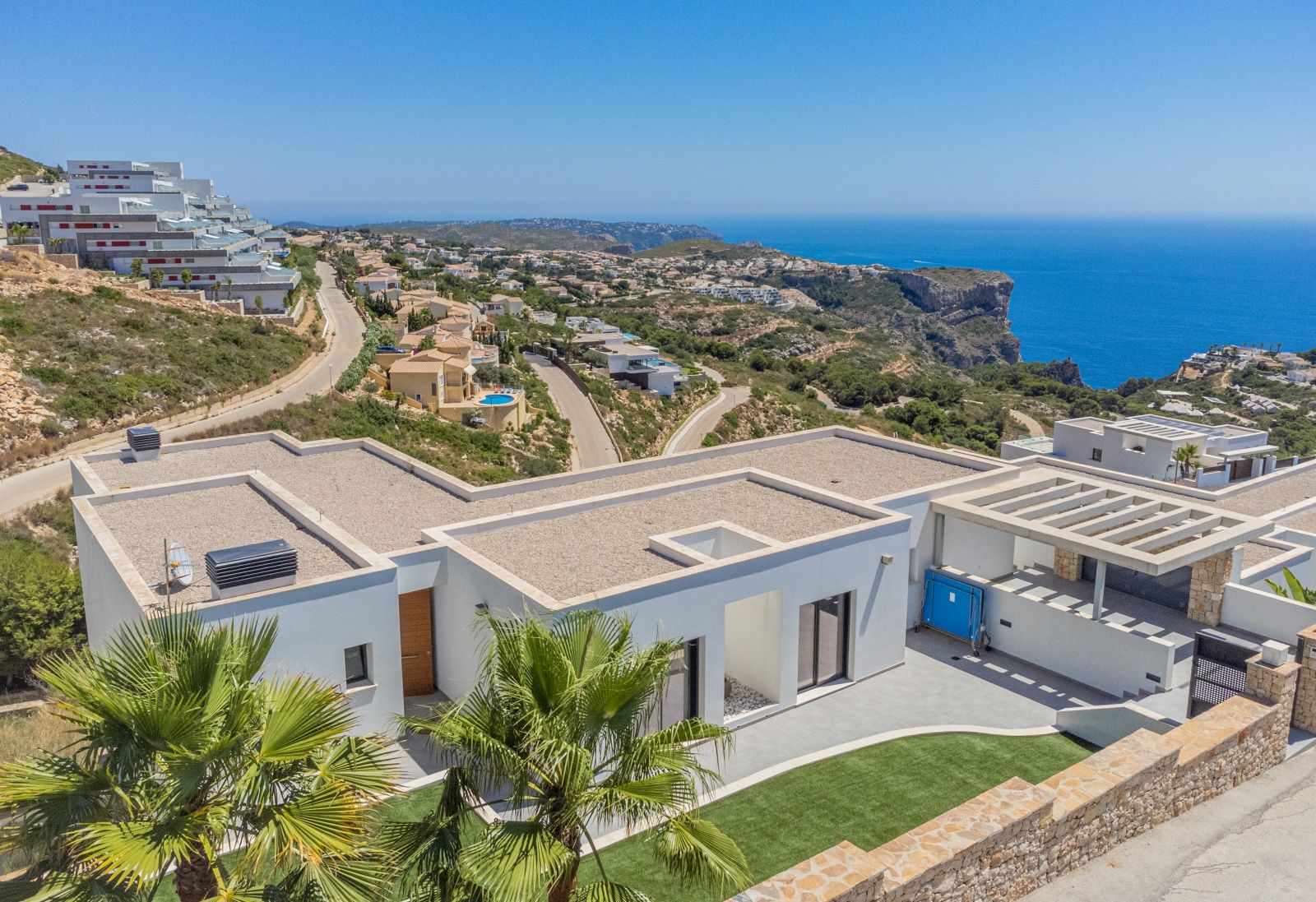 Vista aérea de la villa moderna en Cumbre del Sol, destacando su arquitectura de líneas blancas, cubiertas de grava y vistas panorámicas al mar Mediterráneo y los acantilados.