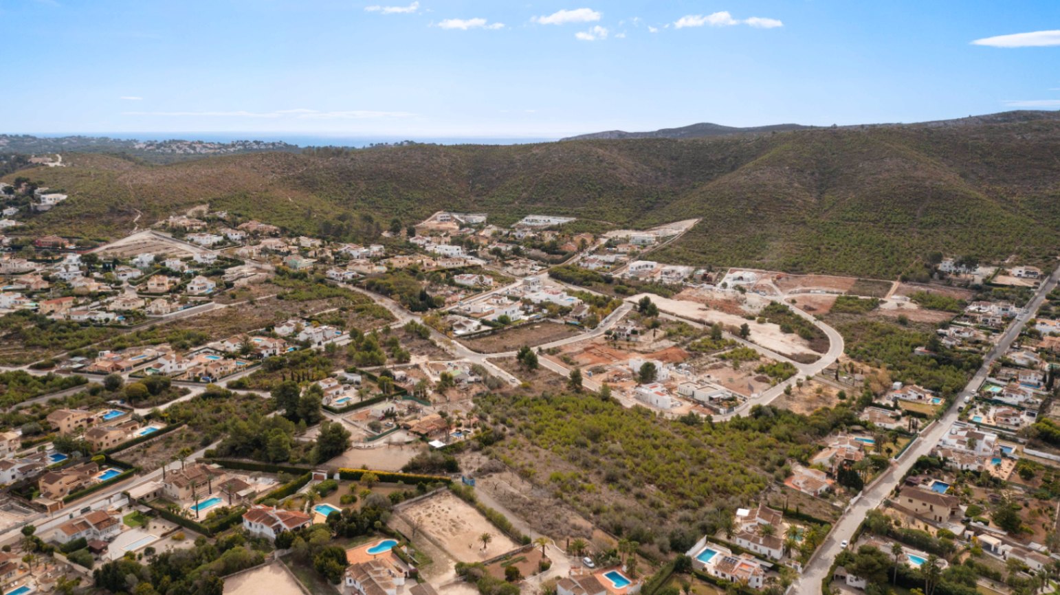 Vista aérea de la urbanización Lomas Del Rey en Jávea, mostrando la integración de las villas con el entorno montañoso y vistas lejanas al mar Mediterráneo.