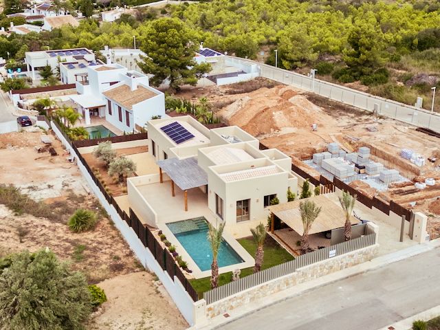 Vista aérea de la villa moderna con paneles solares, piscina rectangular y jardín paisajístico en una parcela vallada rodeada de naturaleza en Jávea.