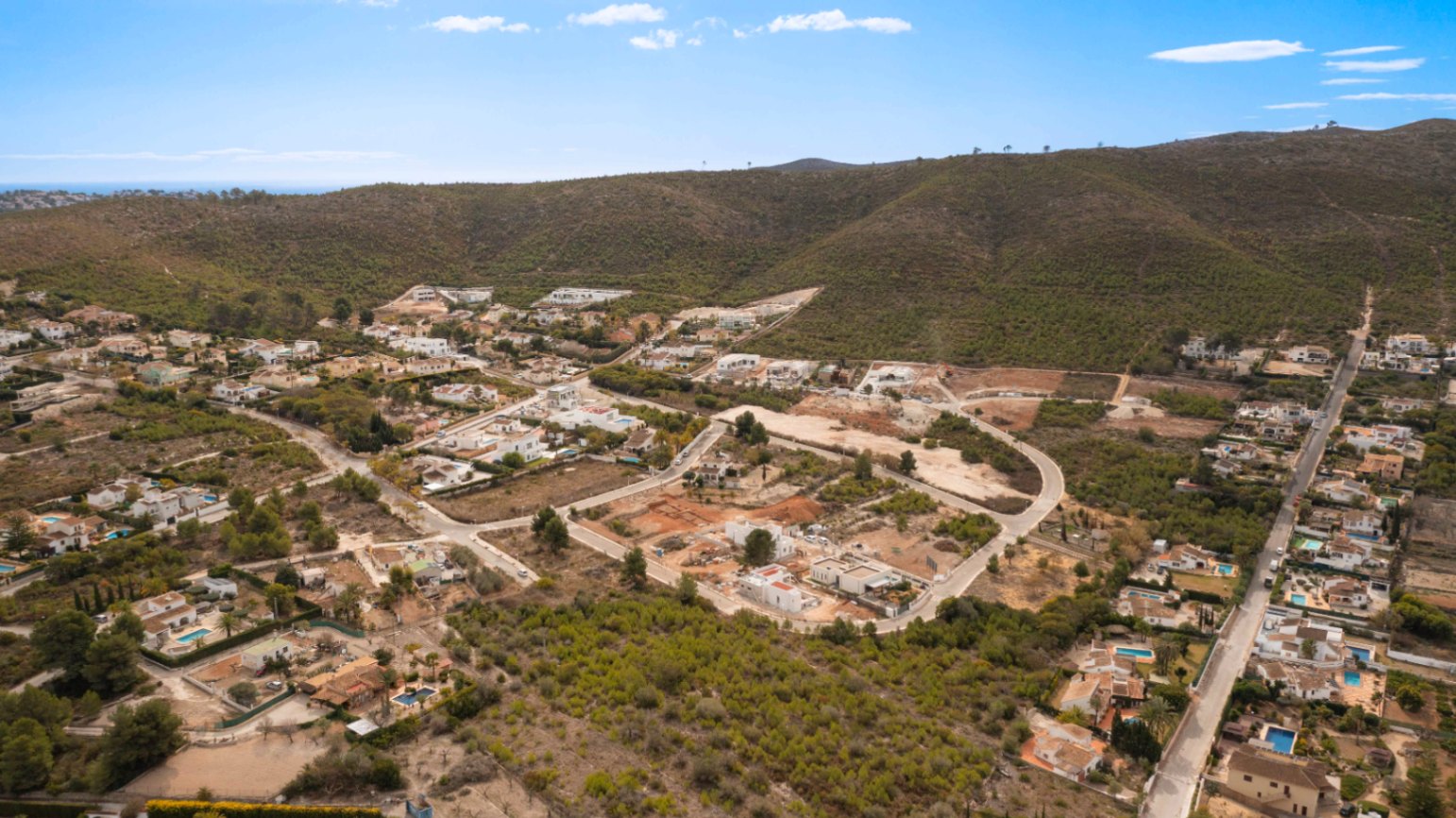 Vista aérea panorámica de la urbanización Lomas Del Rey en Jávea, mostrando la integración de las villas en el paisaje montañoso mediterráneo.