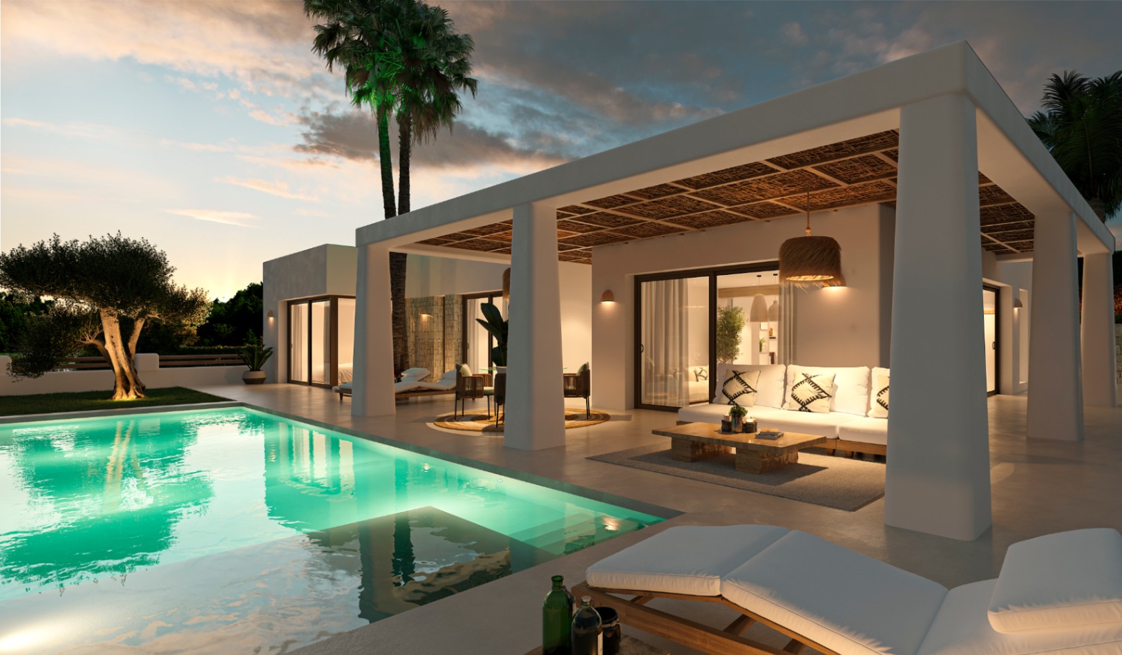 Terraza cubierta de estilo ibicenco con techo de cañizo, zona de estar exterior y piscina iluminada rodeada de vegetación mediterránea al atardecer.