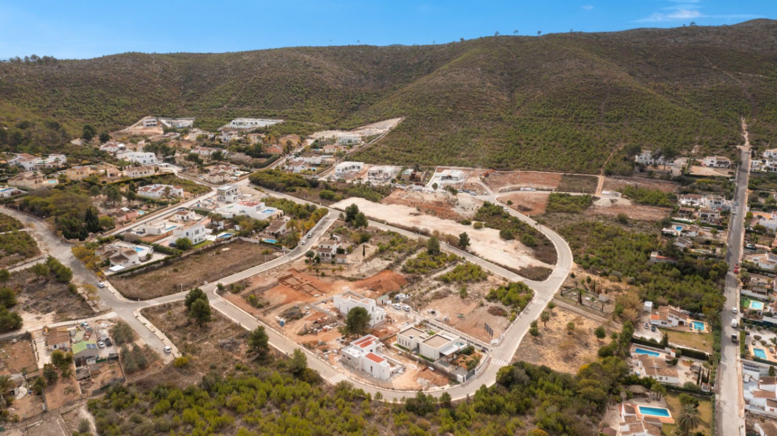 Vista aérea de la urbanización Lomas Del Rey en Jávea, mostrando las parcelas disponibles y viviendas en construcción junto a la ladera de la montaña.