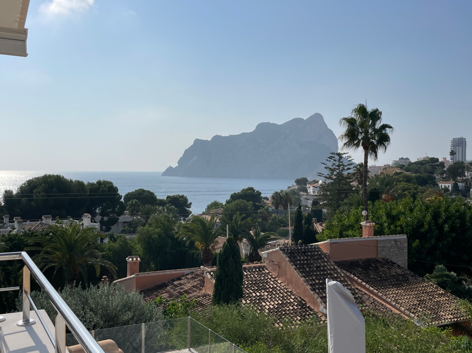 Vista panorámica desde la terraza hacia el Peñón de Ifach y el mar Mediterráneo, rodeada de vegetación local y tejados tradicionales en Calpe.