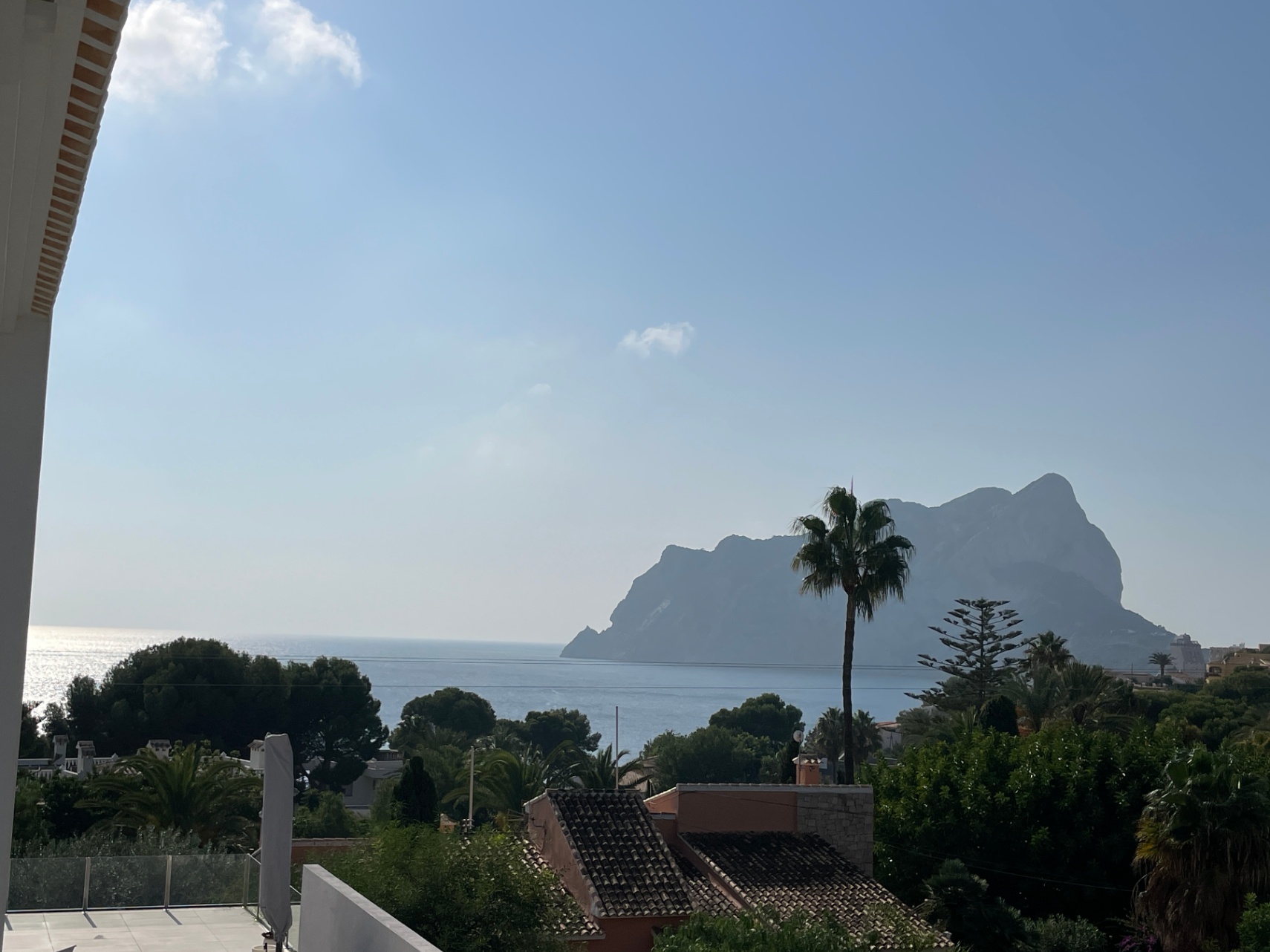 Vistas panorámicas al mar Mediterráneo y al Peñón de Ifach desde una terraza elevada con barandillas de cristal y entorno residencial arbolado.