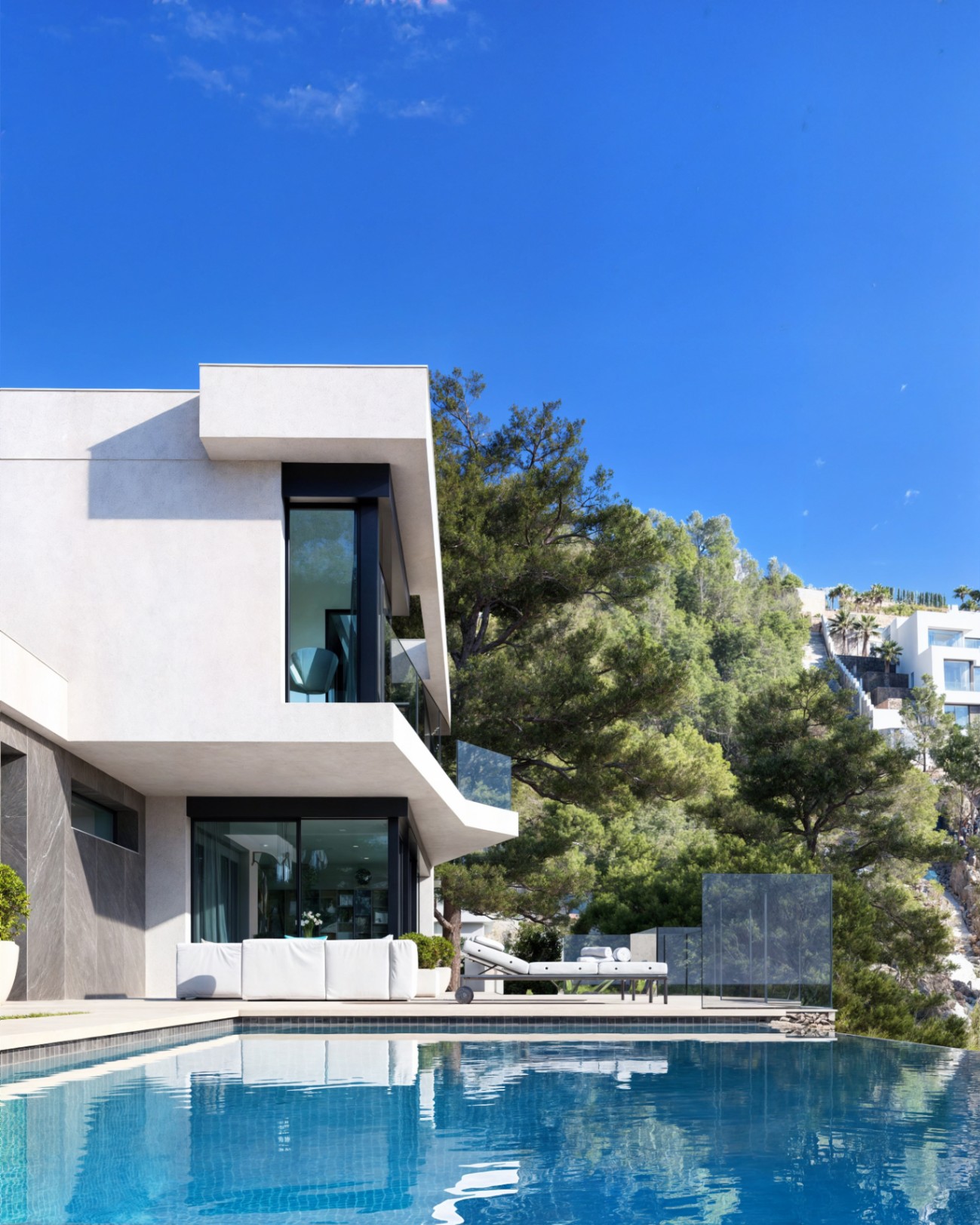 Fachada moderna con piscina infinity, terraza con mobiliario de exterior y ventanales de suelo a techo integrados en un entorno de pinos mediterráneos.