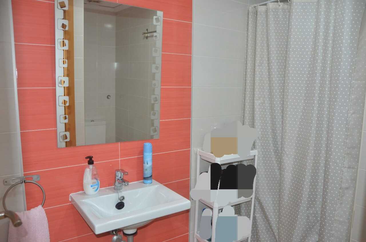 Baño con azulejos en tono coral, lavabo de cerámica blanca y espejo con marco decorativo junto a una cortina de ducha de lunares.