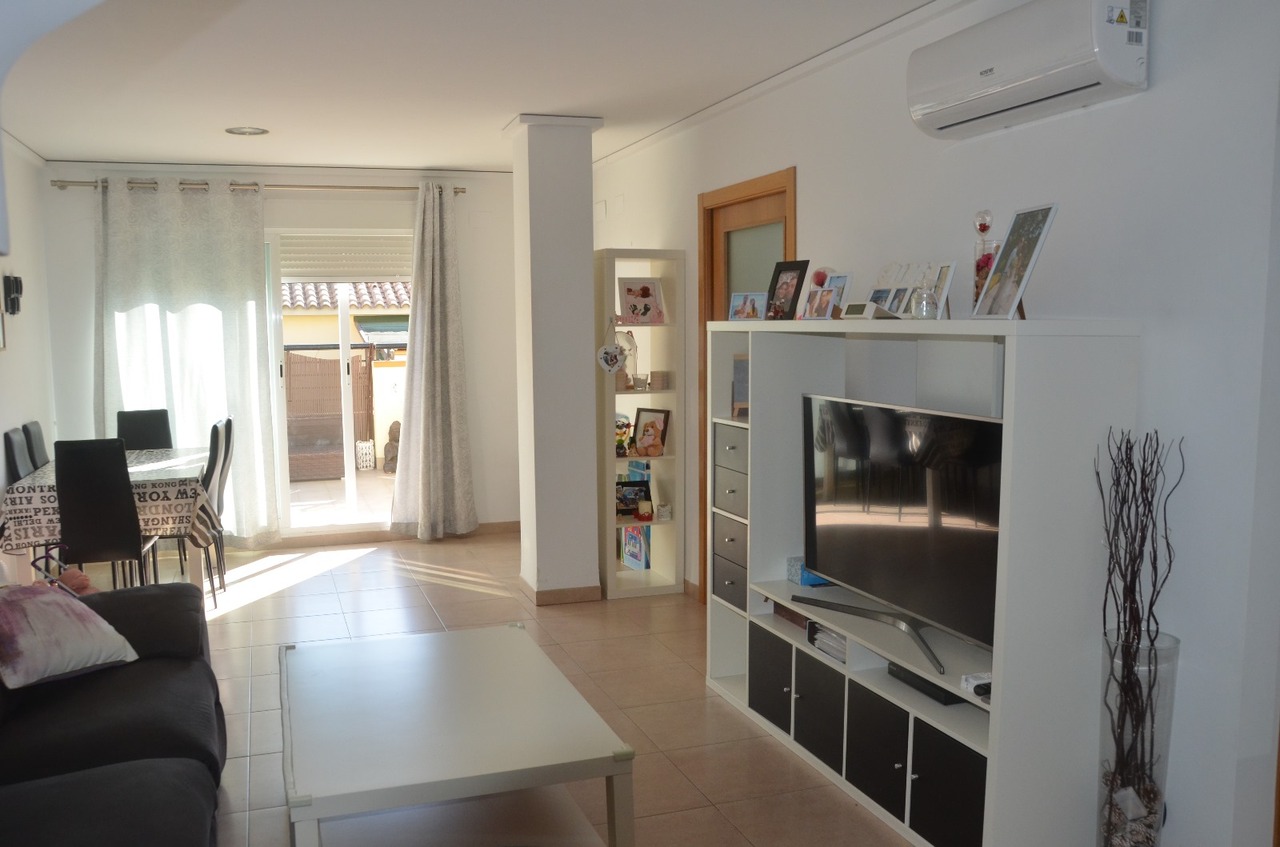 Salón comedor luminoso con suelos cerámicos, mueble de televisión modular en blanco y negro, aire acondicionado y acceso directo a la terraza exterior.
