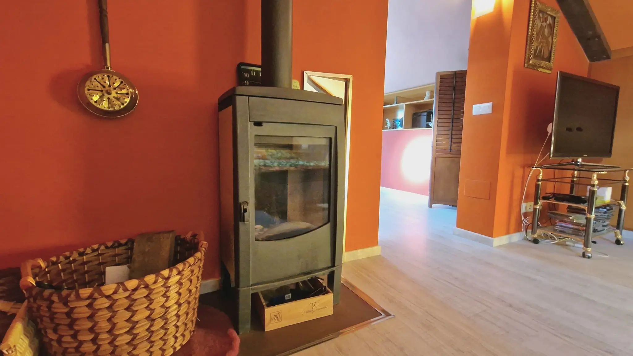 Estufa de leña moderna de color negro integrada en un salón con paredes en tono terracota, suelos de madera clara y cesta de mimbre artesanal.
