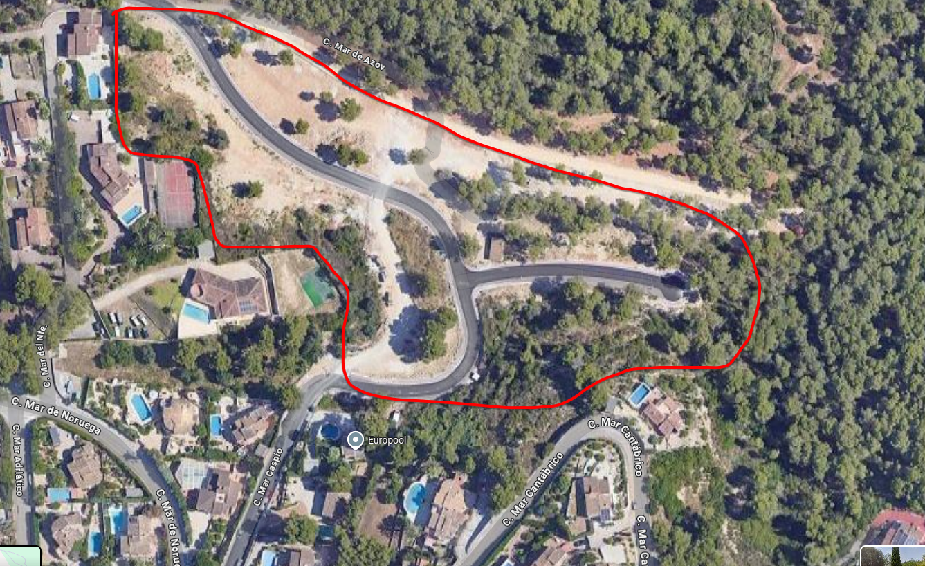 Vista aérea de una parcela urbanizable delimitada en rojo, con viales asfaltados y vegetación mediterránea, rodeada de villas residenciales con piscinas.