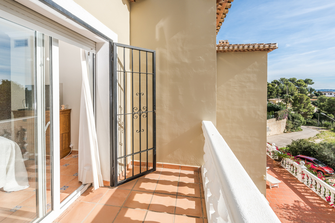 Balcón privado con suelo de terracota y barandilla blanca, equipado con reja de seguridad de hierro forjado y vistas al entorno natural mediterráneo.