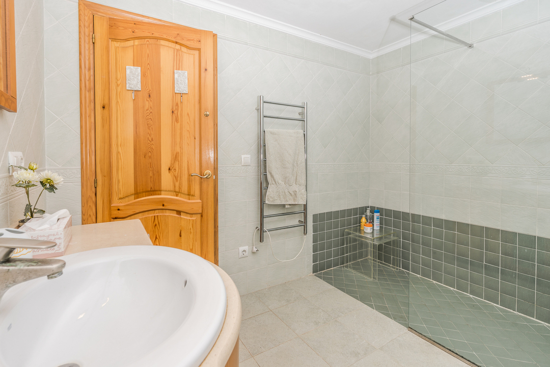 Baño con ducha a ras de suelo, azulejos verdes, mampara de cristal y radiador toallero cromado junto a una puerta de madera maciza.