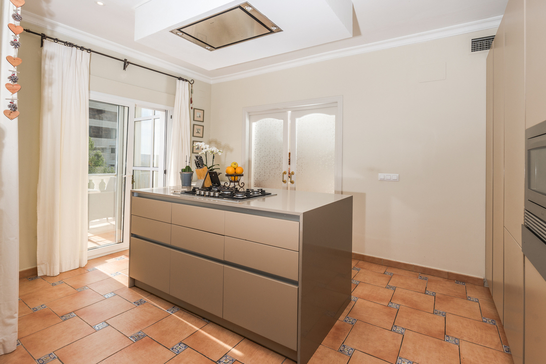 Cocina con isla central, placa de gas, suelo de terracota con detalles decorativos y acceso directo a la terraza exterior.