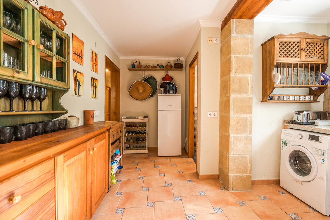 Cocina de estilo rústico con armarios de madera, suelos de baldosas de terracota decoradas, un pilar de piedra vista y zona de lavandería integrada.