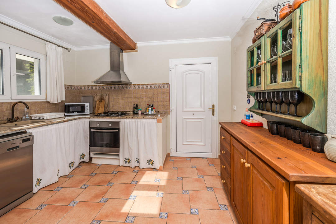 Cocina de estilo rústico con suelos de barro cocido, vigas de madera vista, encimeras de granito y un aparador de madera con vitrina verde.